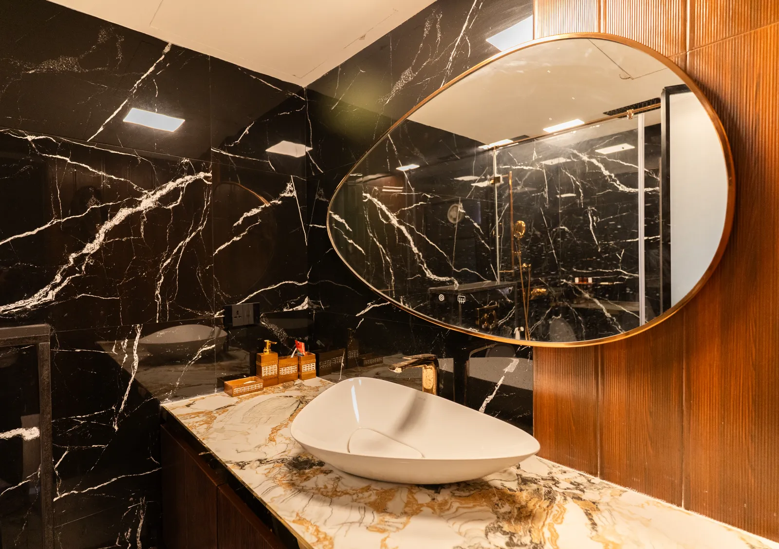 Powder room with black marble walls, oval gold mirror and vessel basin — Abhishek's Residence